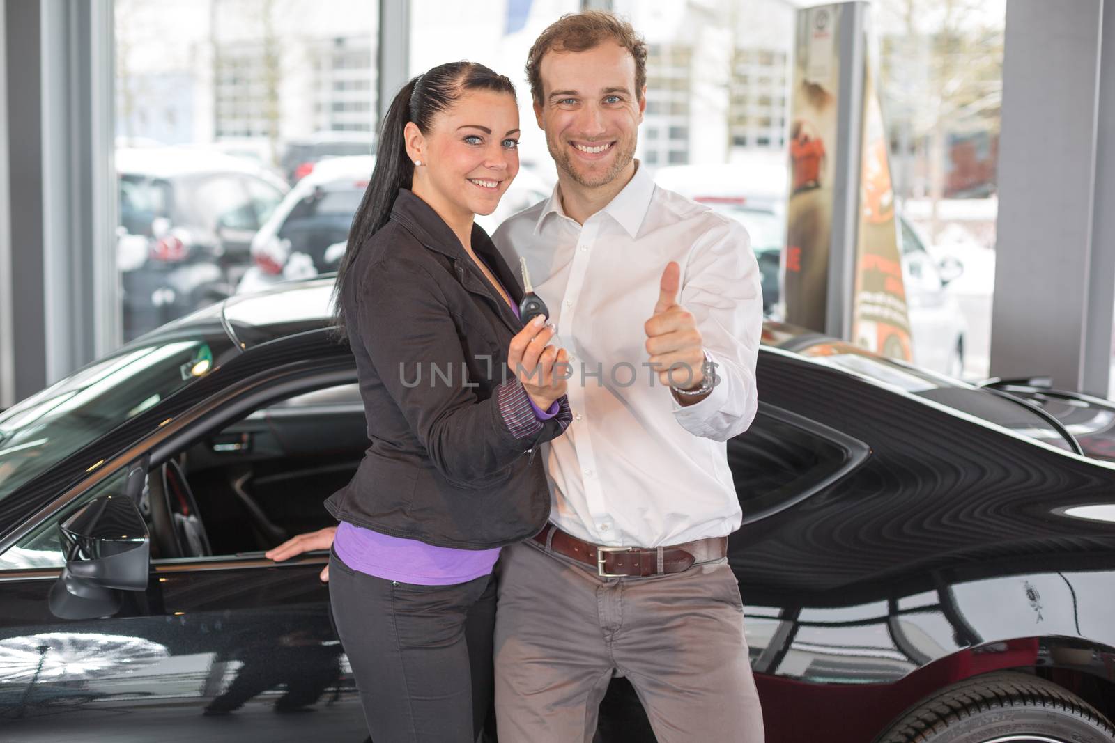 Happy couple with car key in dealership by ikonoklast_fotografie