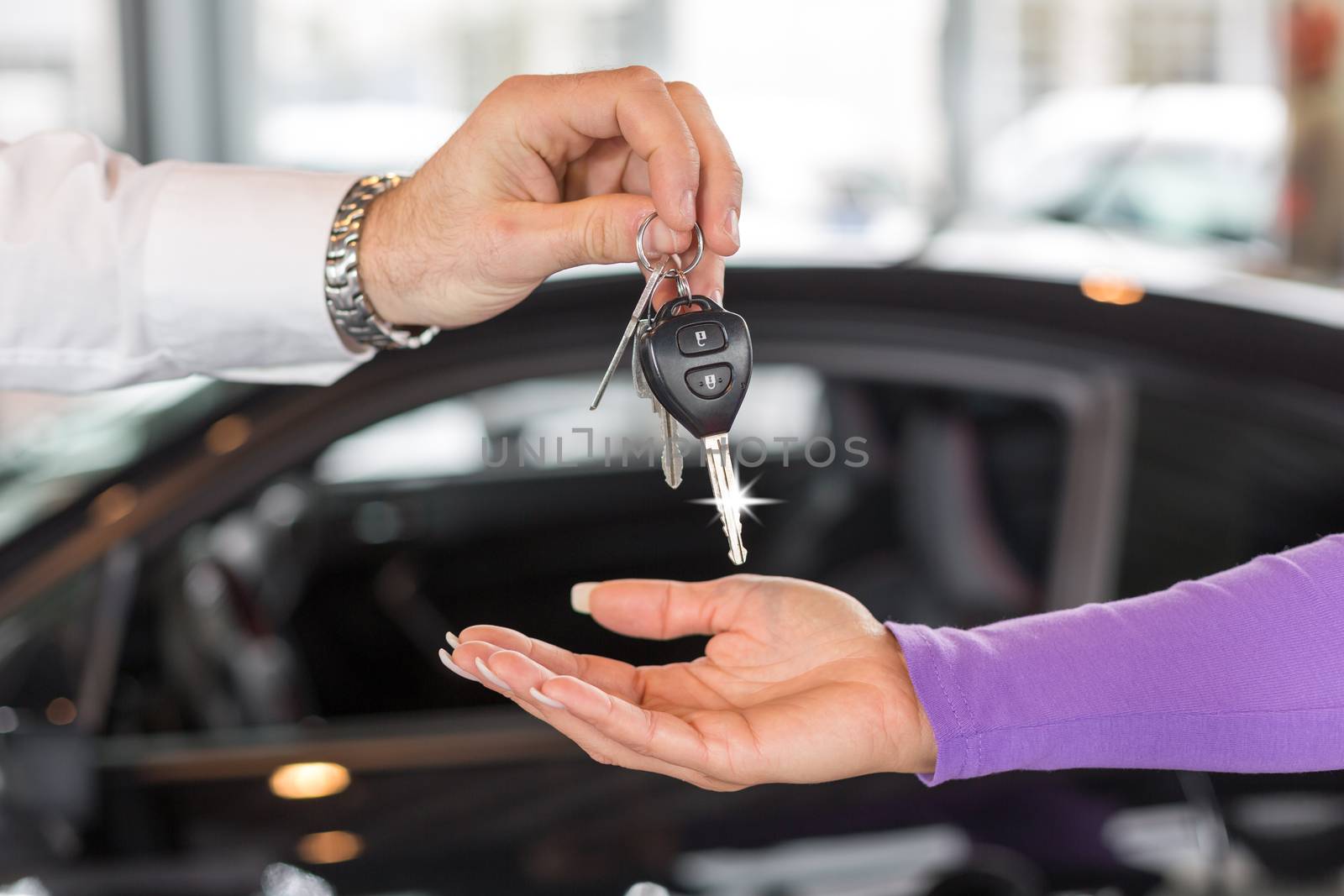 Car salesman handing over car keys in dealership by ikonoklast_fotografie