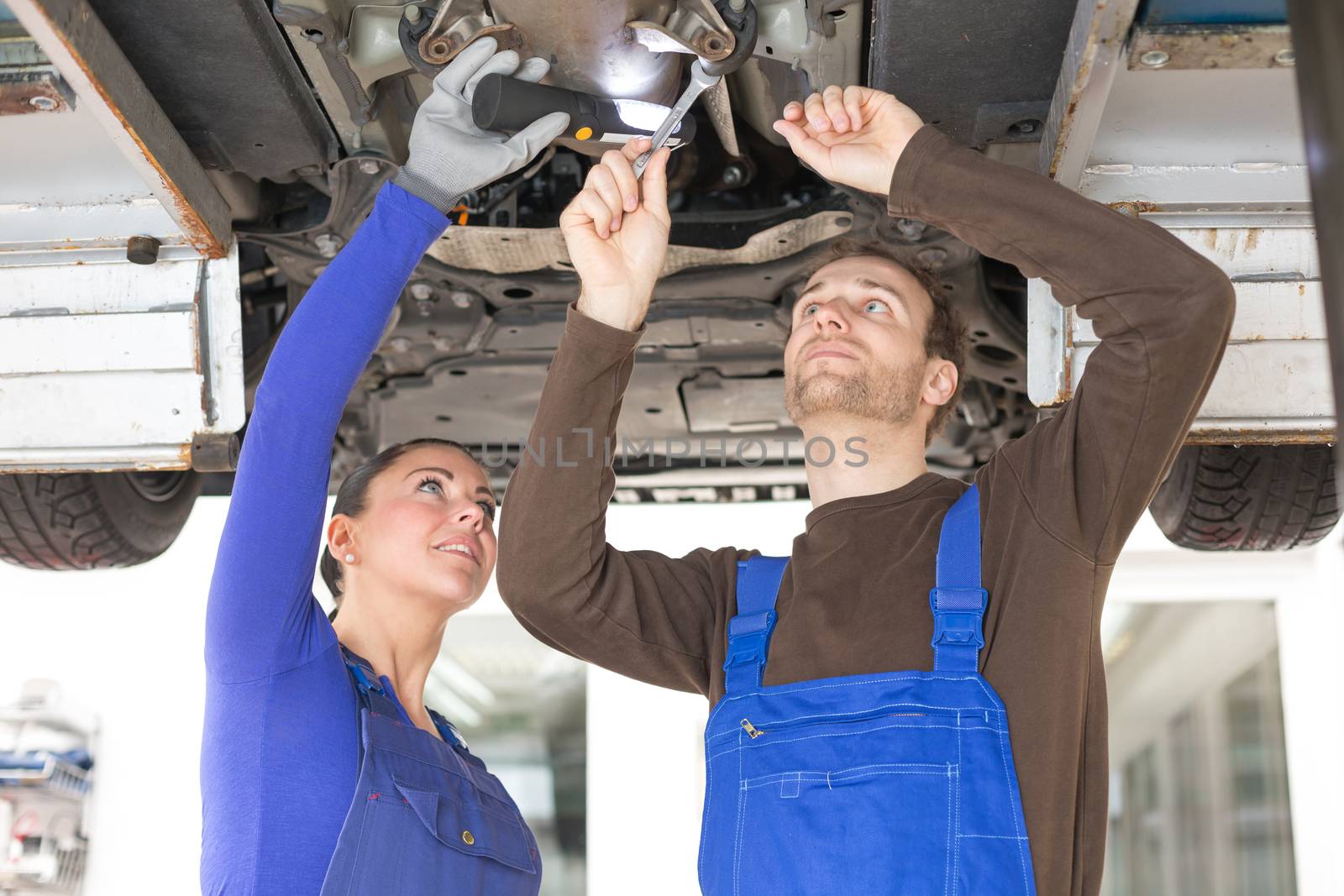 Two mechanics repairing or inspecting a car on hydraulic lift