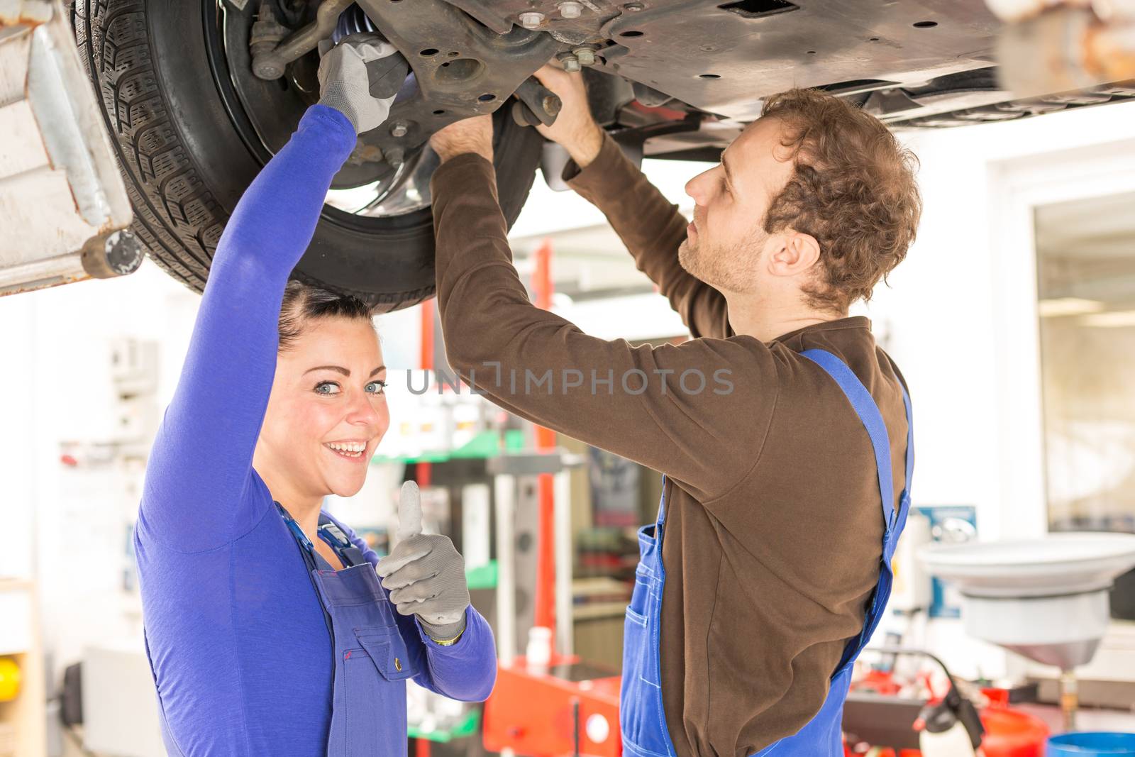 Two mechanics repairing a car in hydraulic lift by ikonoklast_fotografie