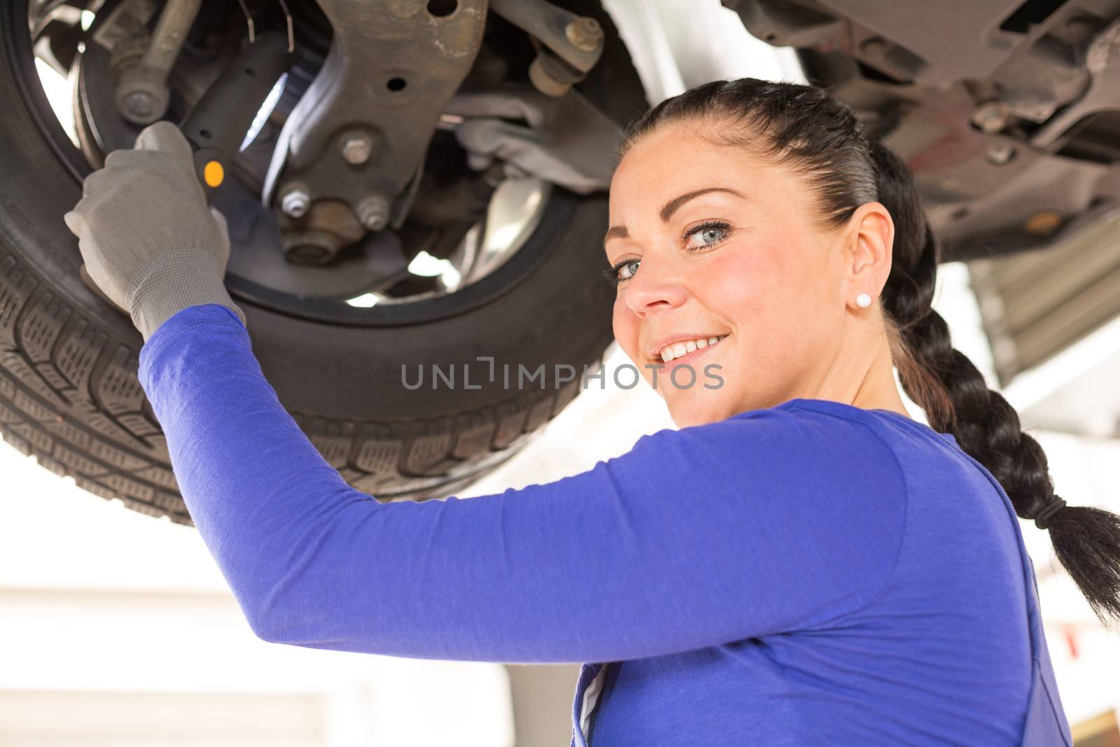 Woman repairing the brakes of a car on hydraulic lift