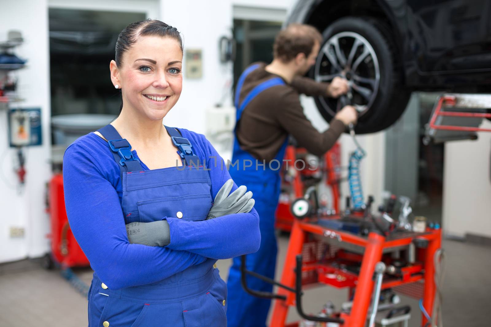 Female mechanic standing in workshop, another mechanic changes a wheel at a car on a hydraulic lift