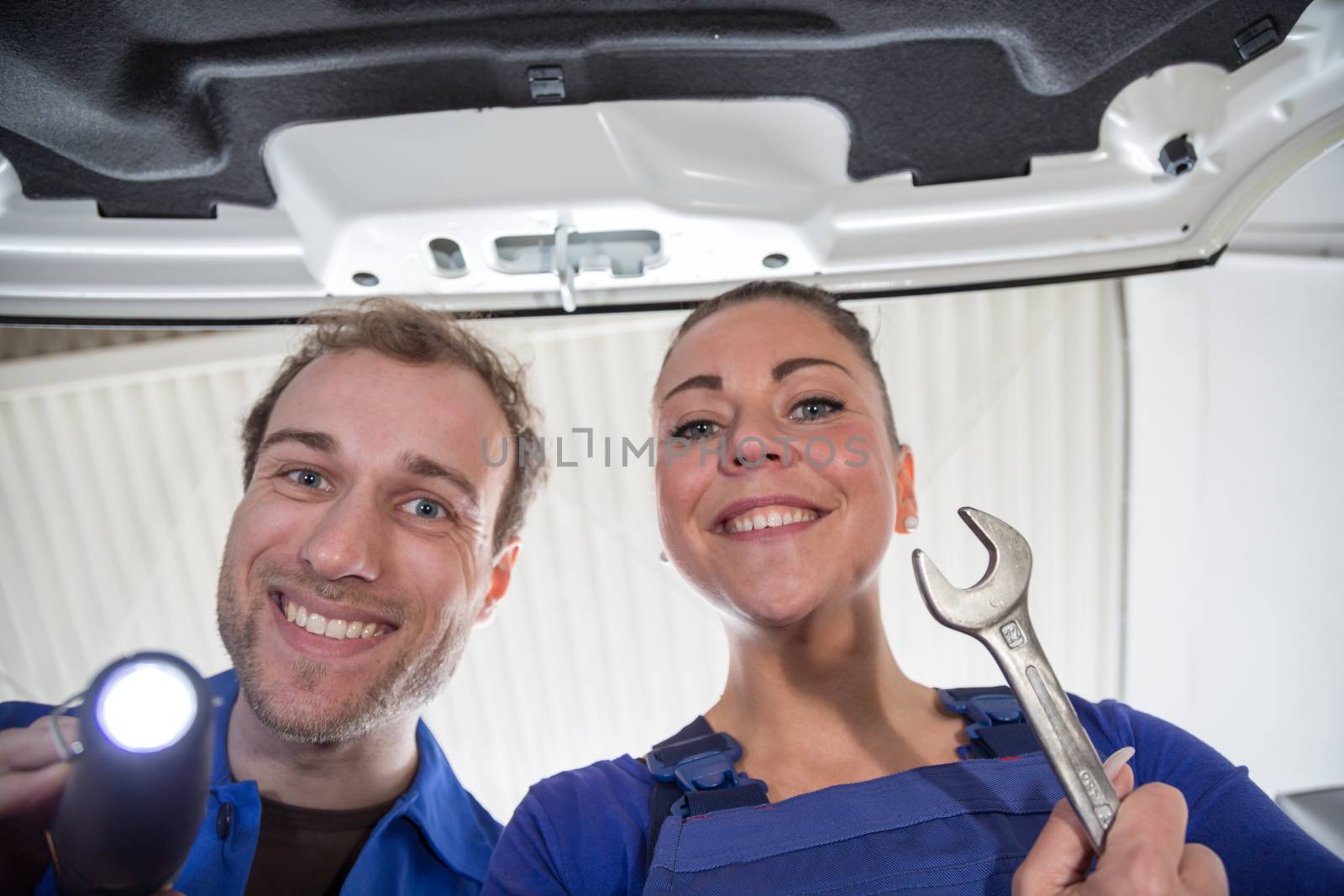 Two mechanics taking a look under the hood of a car in a garage to repair it