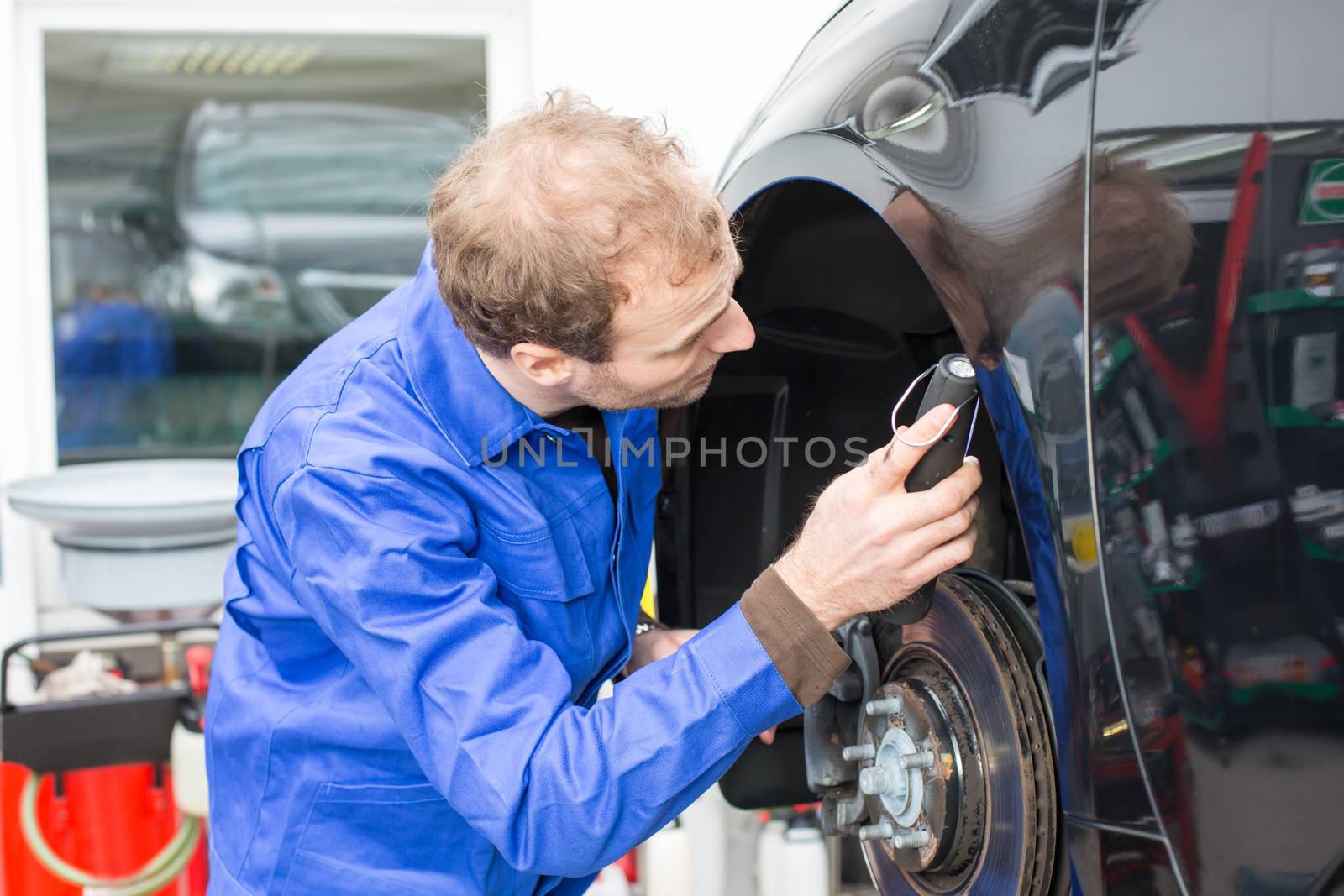 Car mechanic repairs the brakes of an automobile on a hydraulic lift