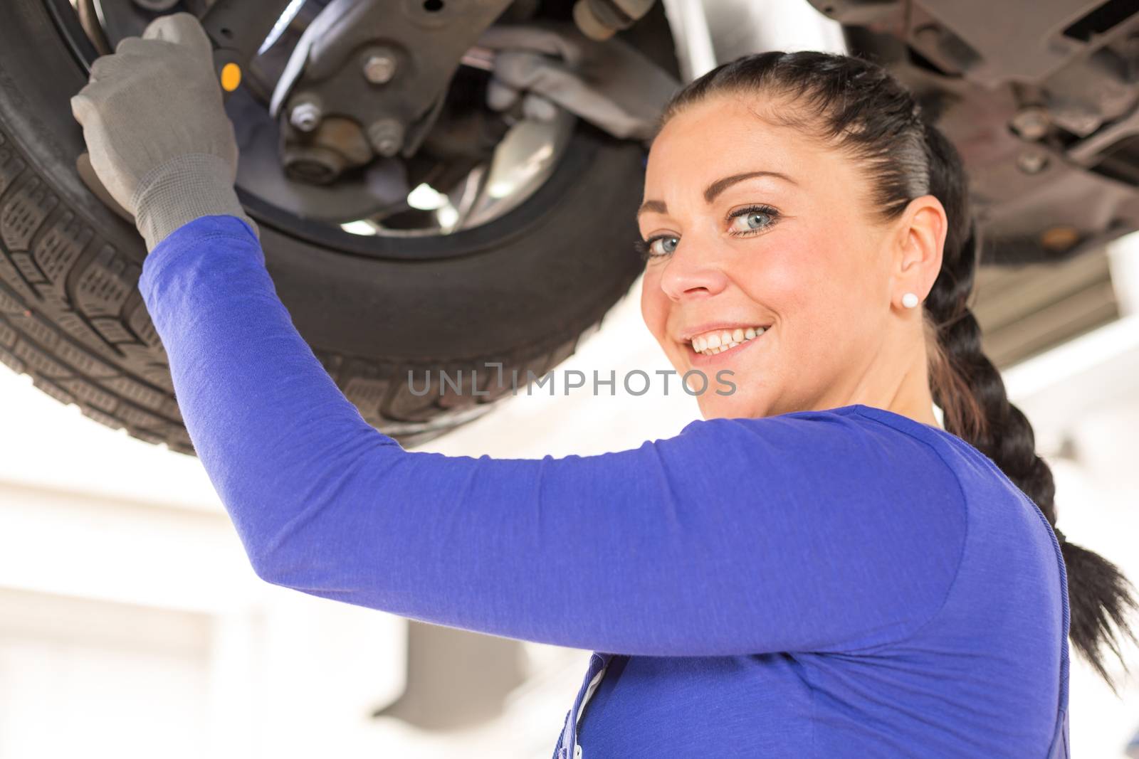 Woman repairing the brakes of a car on hydraulic lift