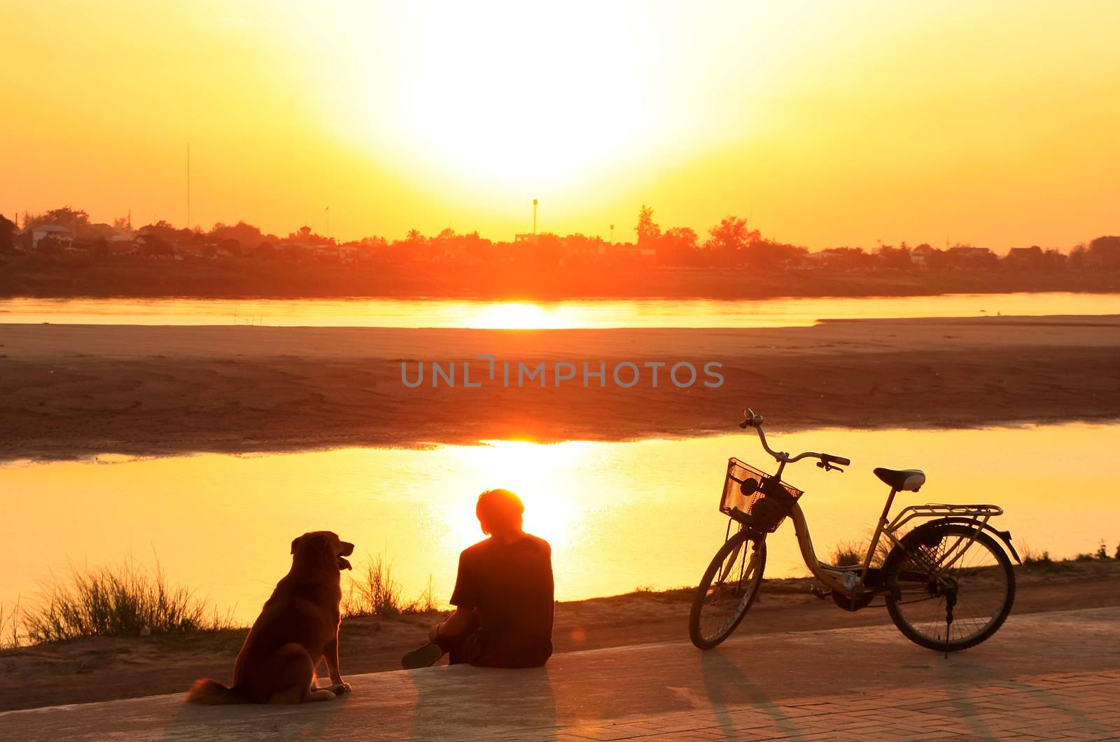 Silhouetted man with a dog watching sunset at Mekong river water by donya_nedomam