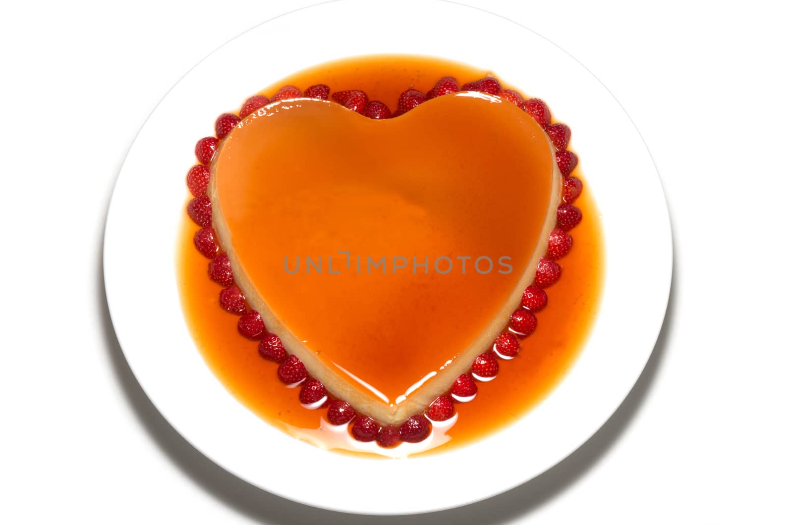 Heart shape flan caramel with strawberries on the edge on white background