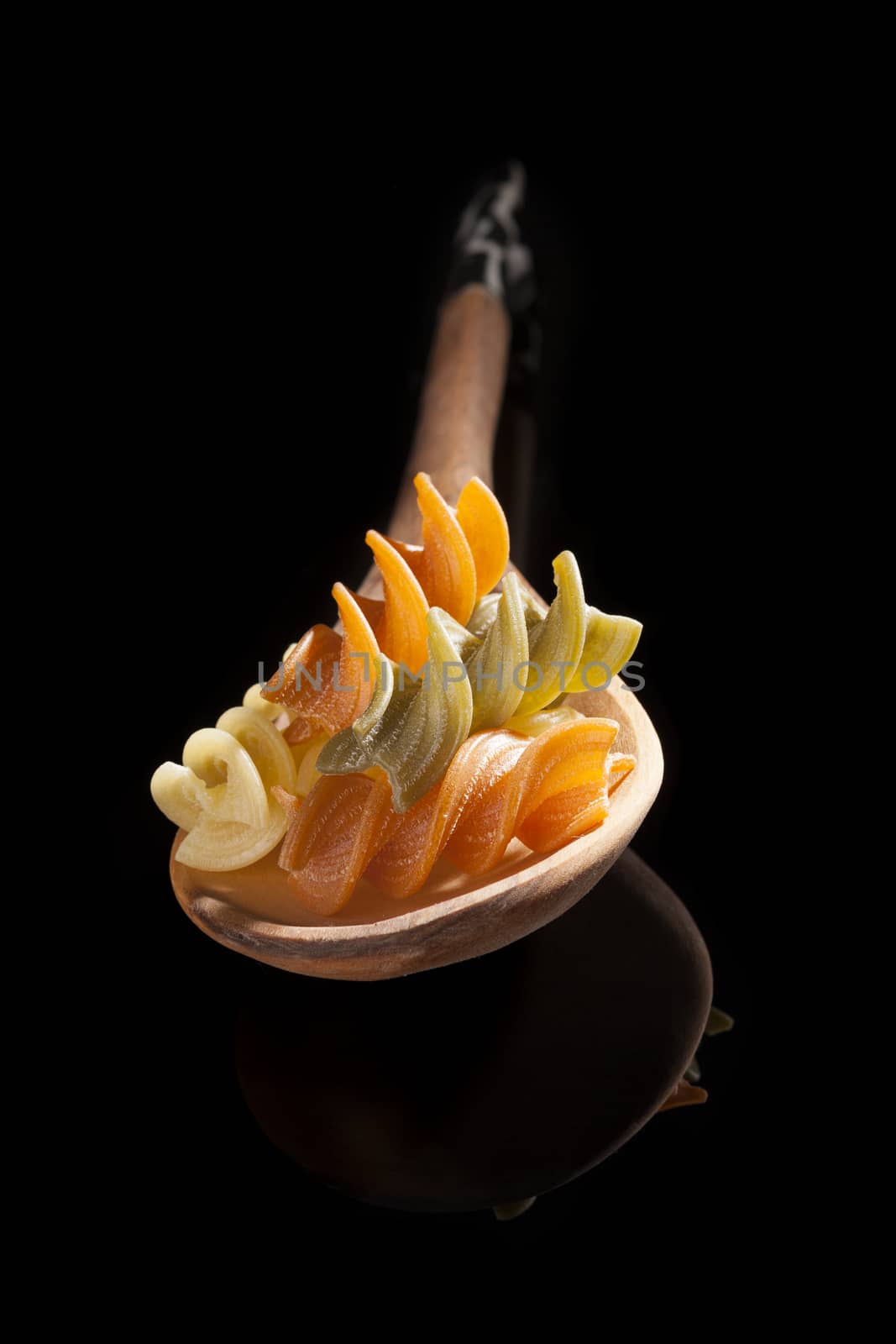 Fusilli on wooden spoon isolated on black background. Culinary pasta cooking background. 