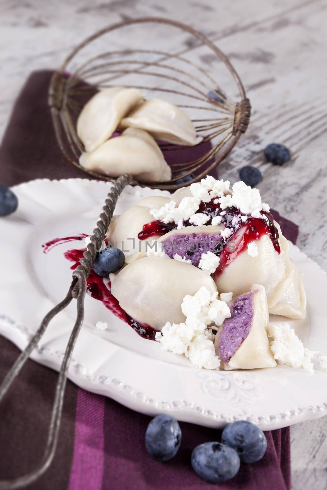 Culinary sweet dessert eating. Blueberry filled dumpling with jam and fresh fruit on plate on white wooden background. Rustic, country style eating.