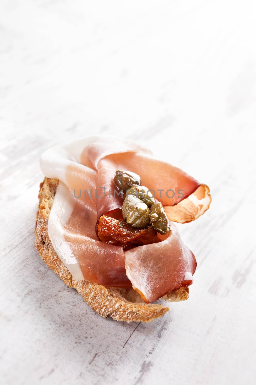 Delicious appetizer background, rustic styles. Traditional tapas. Ciabatta bread with prosciutto ham, dry tomatoes and capers. Fine eating.