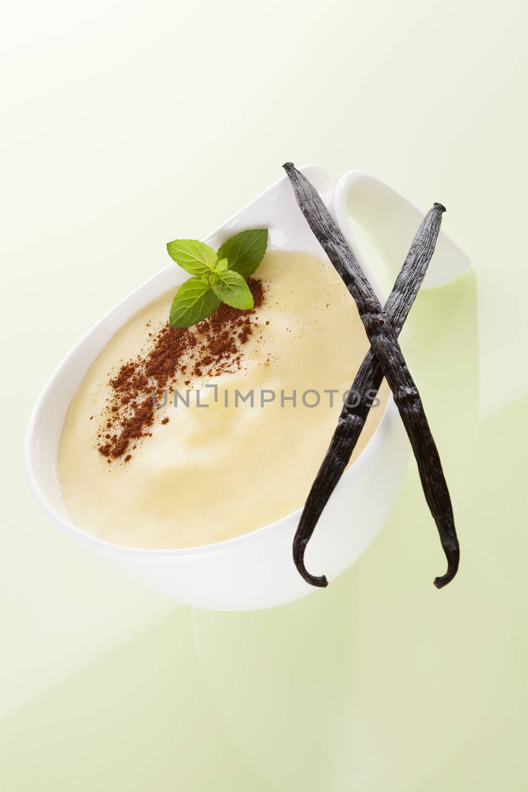 Delicious vanilla pudding with cocoa powder, fresh mint leaves and dry vanilla sticks on yellow background. Culinary sweet dessert eating.