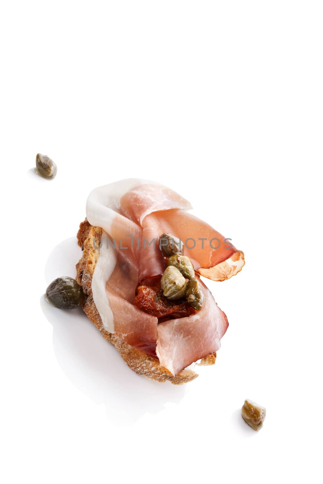 Delicious canape with prosciutto, capers and dry tomatoes isolated over white. Culinary eating.