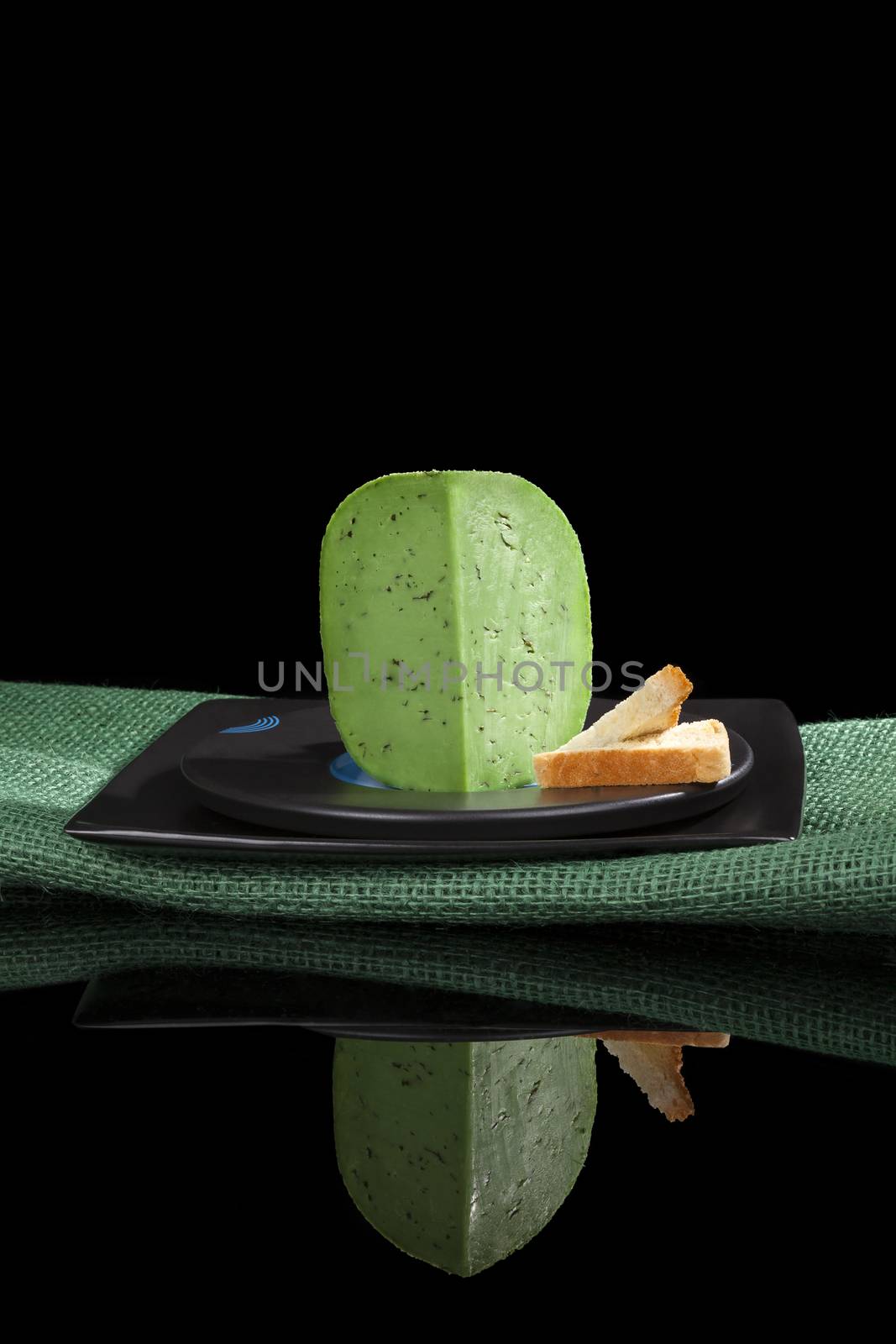 Green gouda on black plate with toast isolated on black background. Luxurious cheese eating.