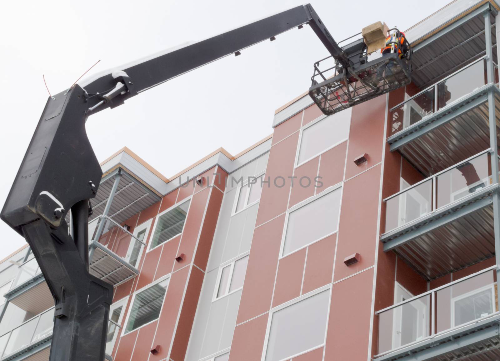 Workmen working on outside of multistorey apartment block using mechanical crane machine with basket on hydraulic extension boom, also called industrial cherry picker