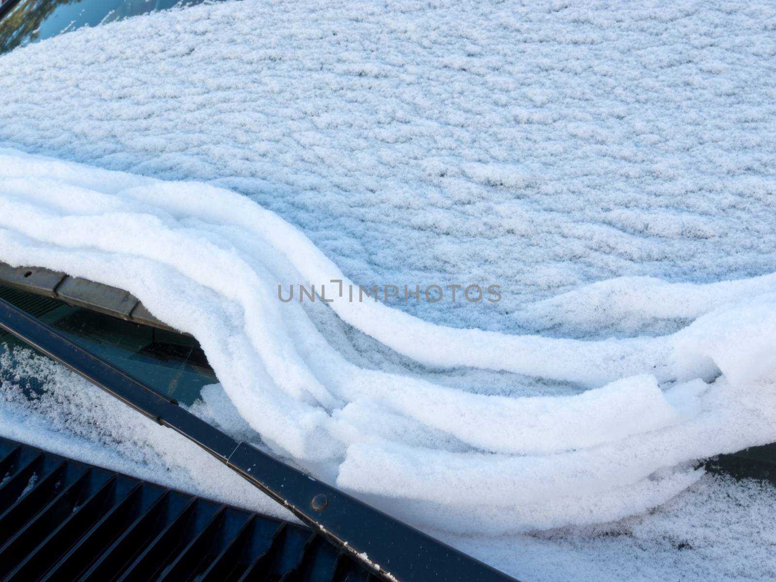 Fresh snow thawing and sliding on vehicle windshield developing ridges and wrinkles