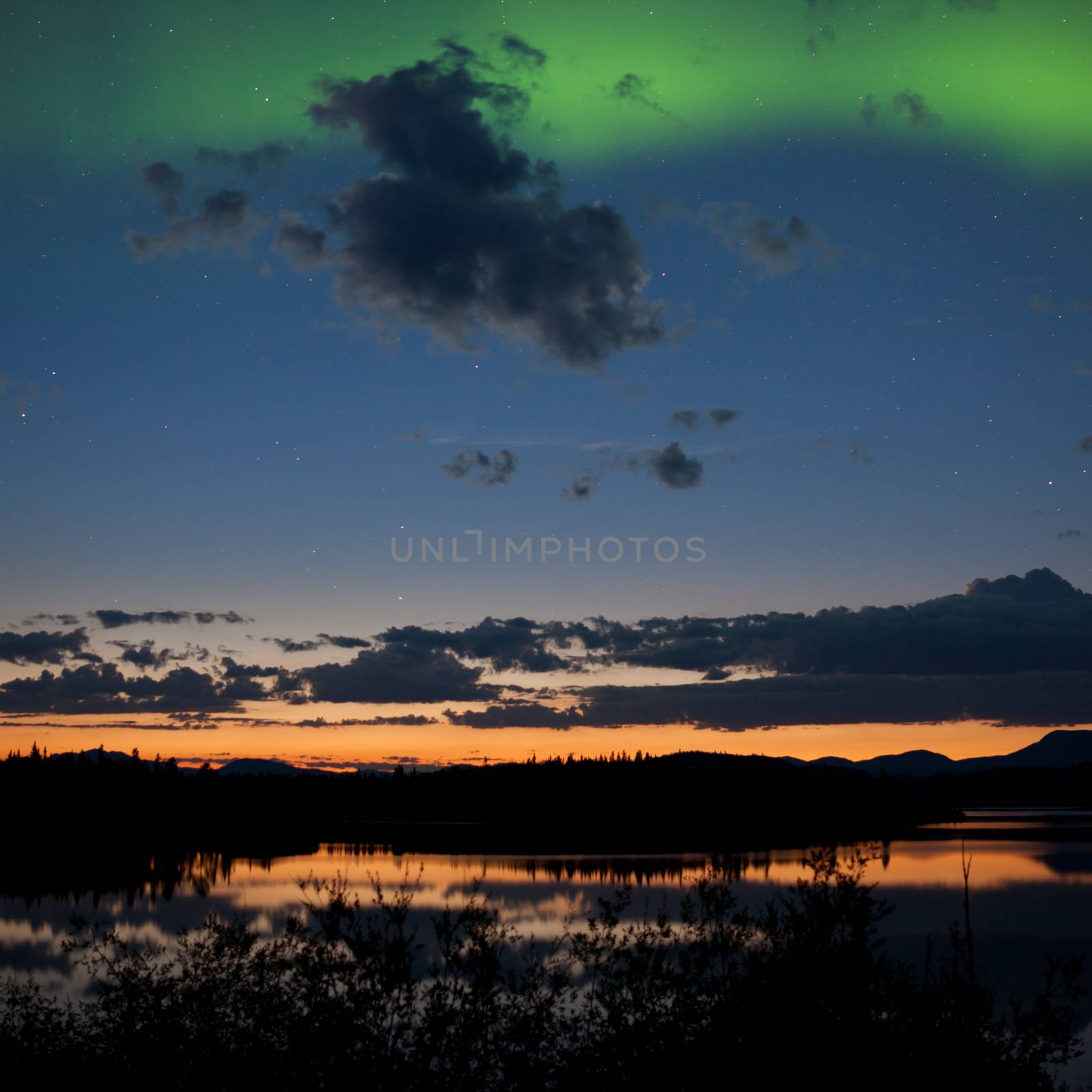 Northern lights Aurora borealis at midnight in summer over northern horizon of Lake Laberge Yukon Territory Canada midnight sun just below