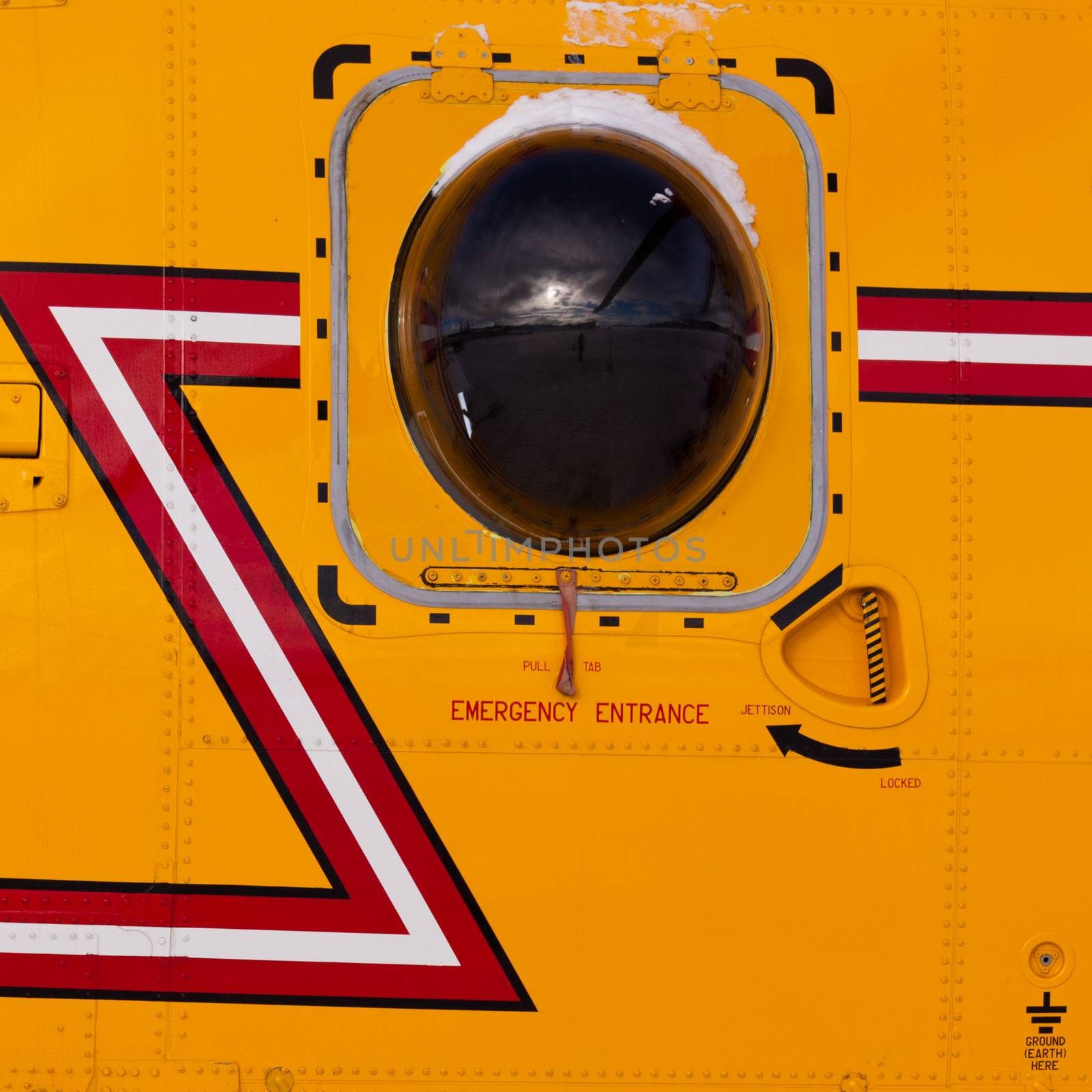 Background detail abstract of emergency hatch bull's-eye porthole of a yellow rescue helicopter reflecting rotor blade and airfield