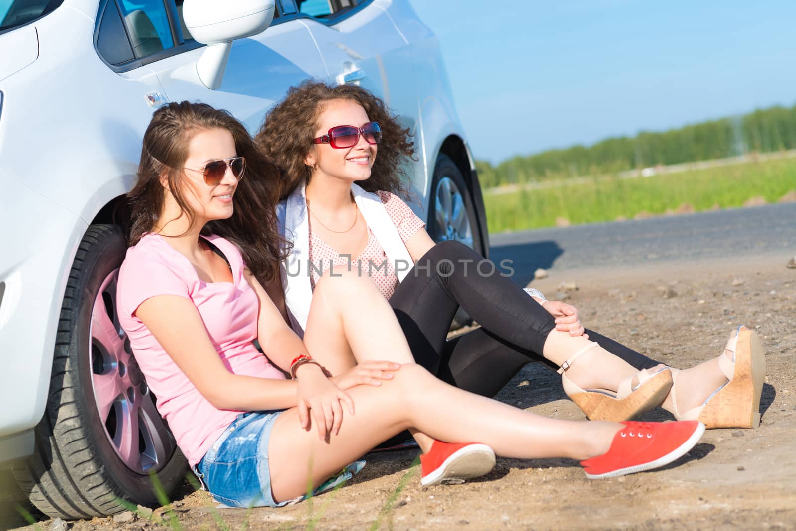 Two attractive young women wearing sunglasses, sitting next to the car