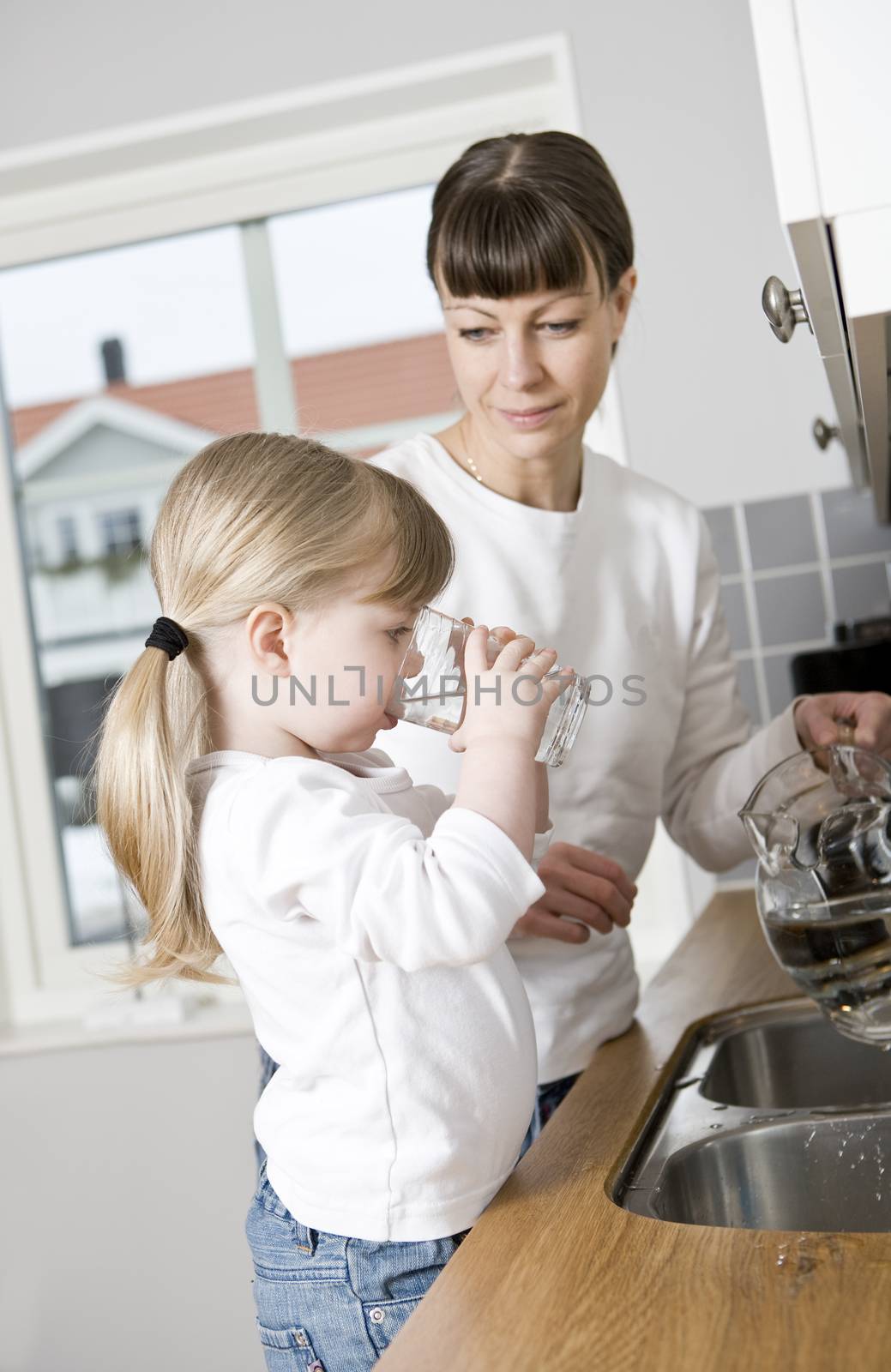 Small Girl in the kitchen with her mother drinking water