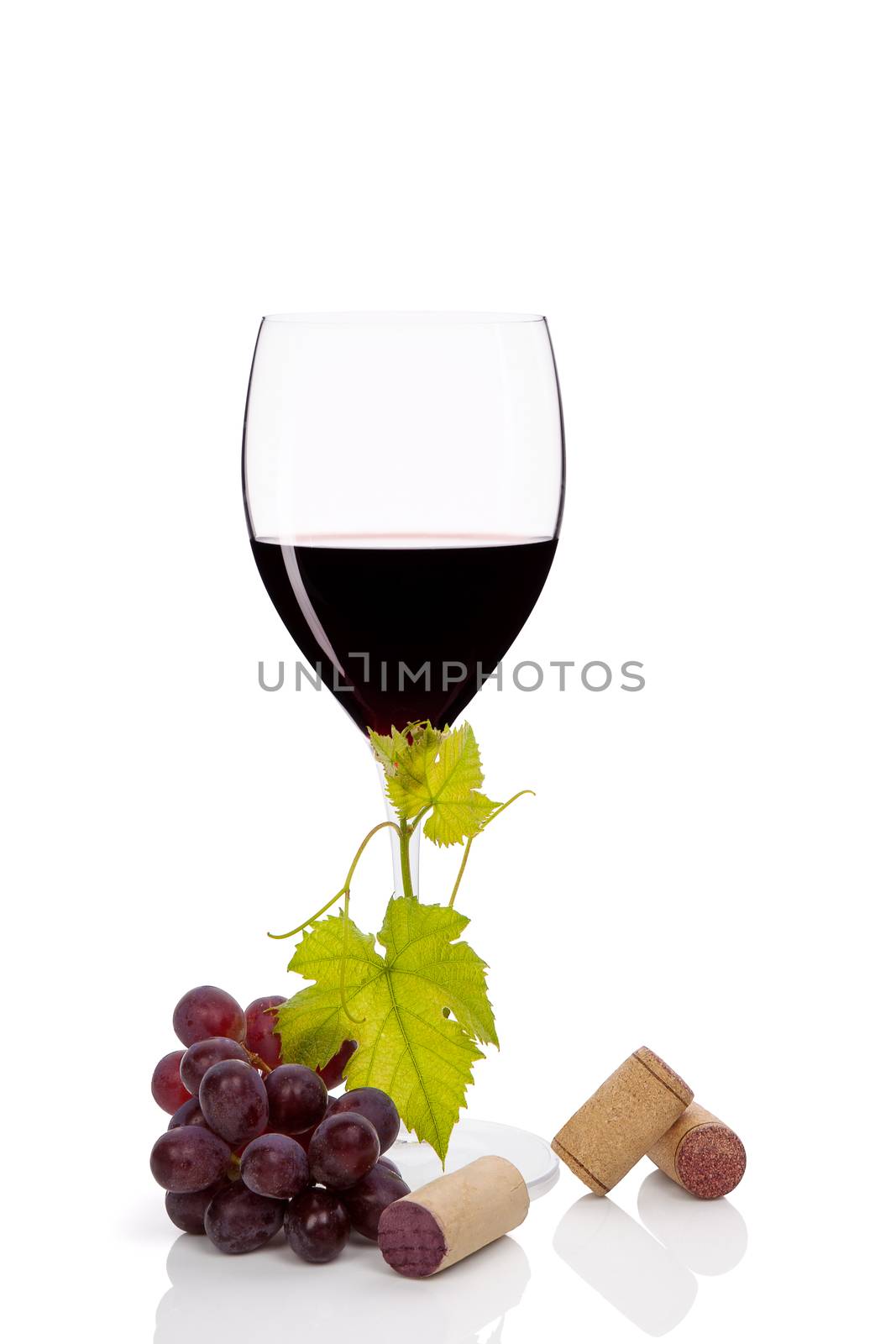 Red wine in wine glass with red grapes and various wine corks isolated on white background. Luxurious wine still life.