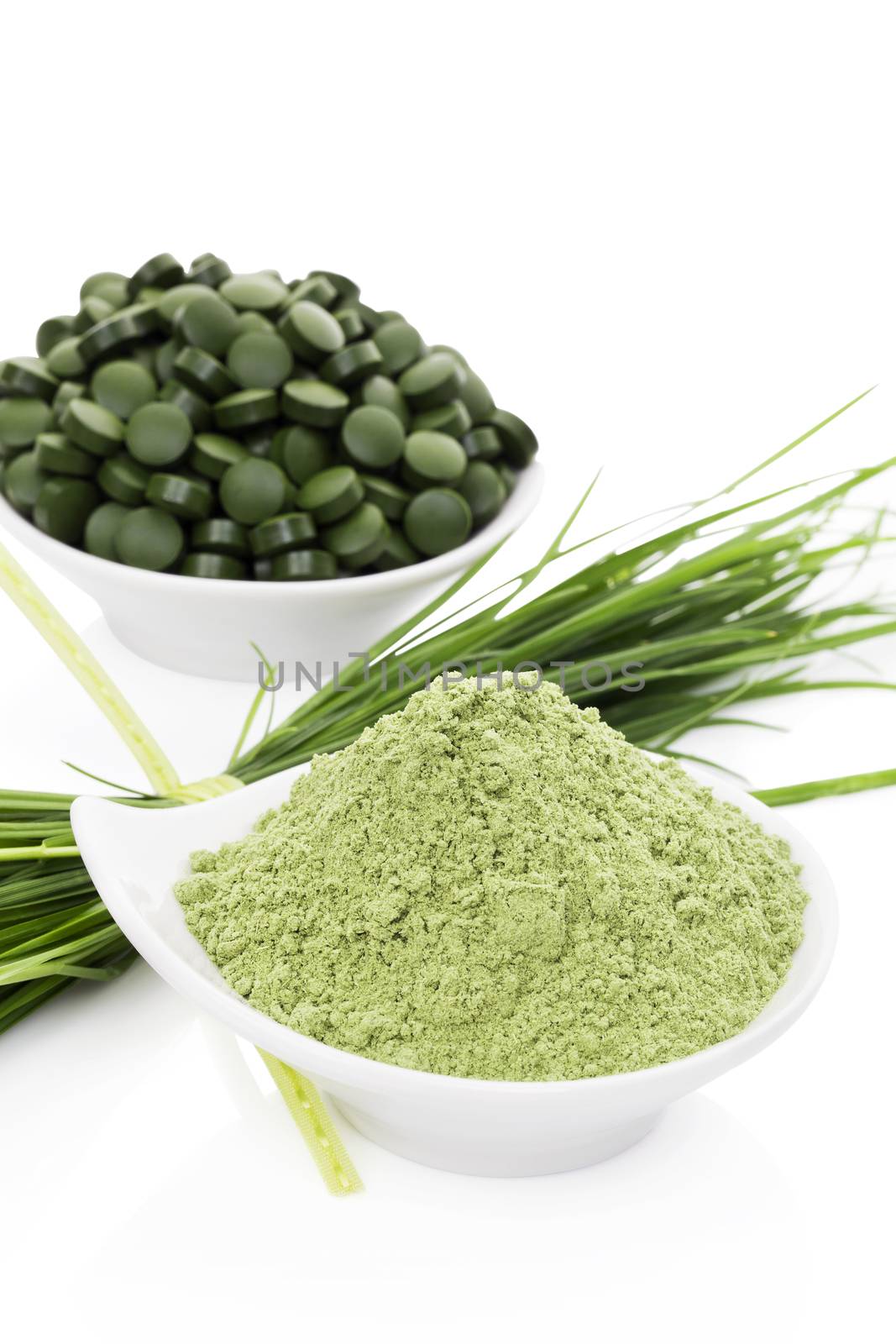 Green food supplement. Spirulina, chlorella and wheatgrass. Green pills, wheatgrass blades and ground powder isolated on white background. Healthy lifestyle.