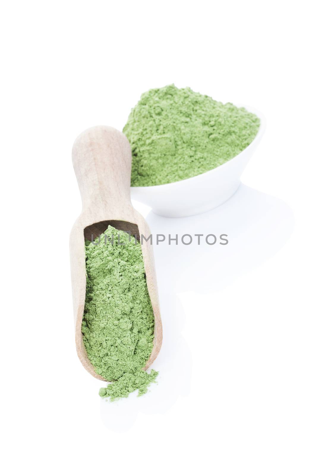 Ground wheat grass in bowl and wooden spoon isolated on white background. Green healthy detox food supplement.