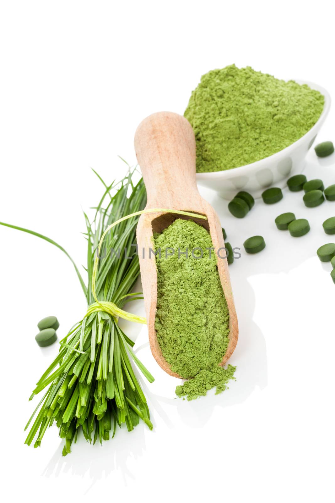 Natural herbal organic alternative medicine. Superfood. Wheatgrass powder, blades and green pills on wooden scoop and white bowl isolated on white. Healthy lifestyle.