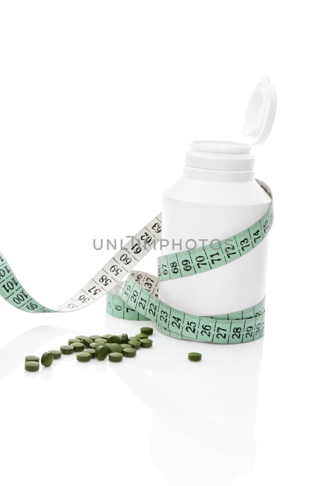 White pill bottle, measurement tape and green chlorella and spirulina pills isolated on white background. Natural healthy living. Detox a diet concept.