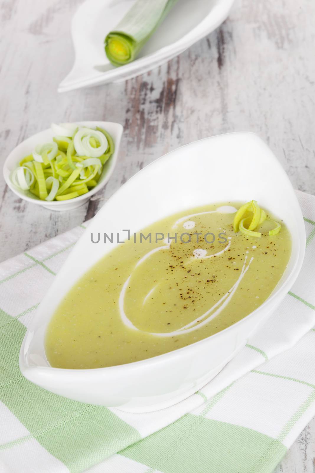 Tasty leek soup in modern white bowl on white wooden textured background. Culinary tasty soup appetizer concept.