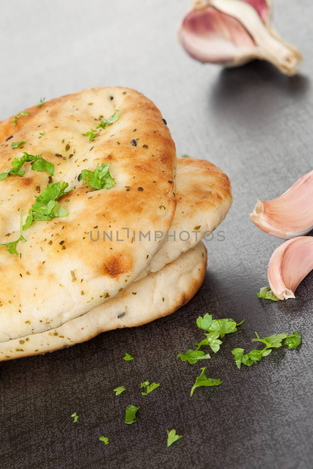 Naan flatbread stack with fresh cilantro herb and garlic on dark black and grey background. Culinary eastern background.