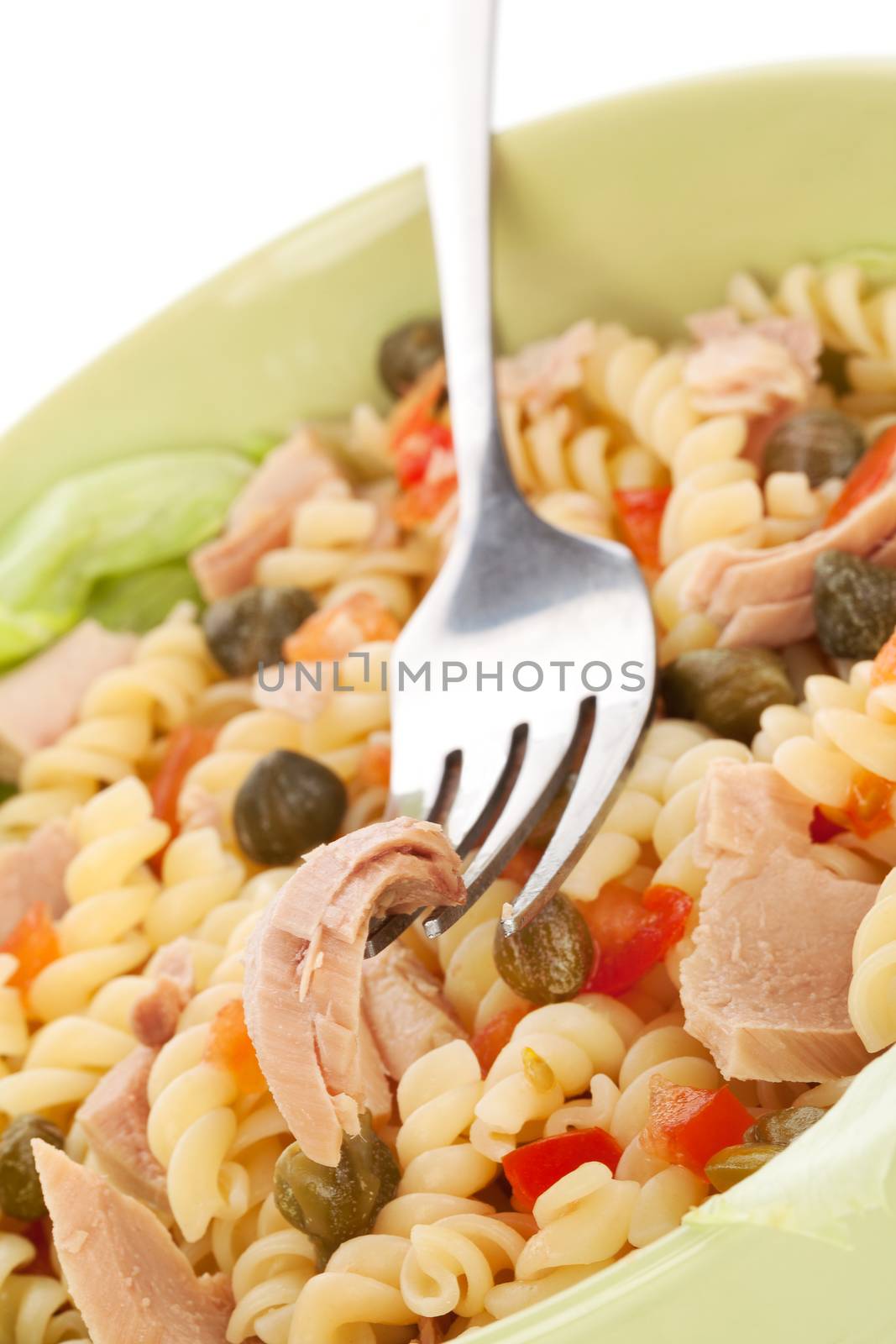 Delicious pasta with tuna, capers and vegetable in green bowl. Tuna piece on fork. Culinary eating.