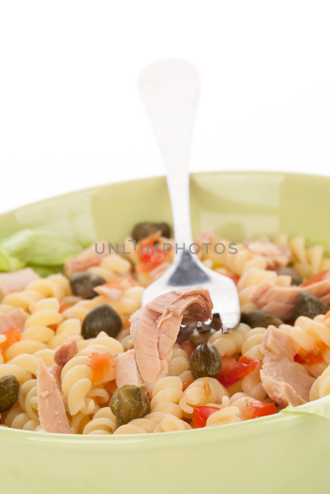 Tuna salad with tuna pieces, capers, and fusilli in green bowl. Tuna piece on fork. Culinary eating.