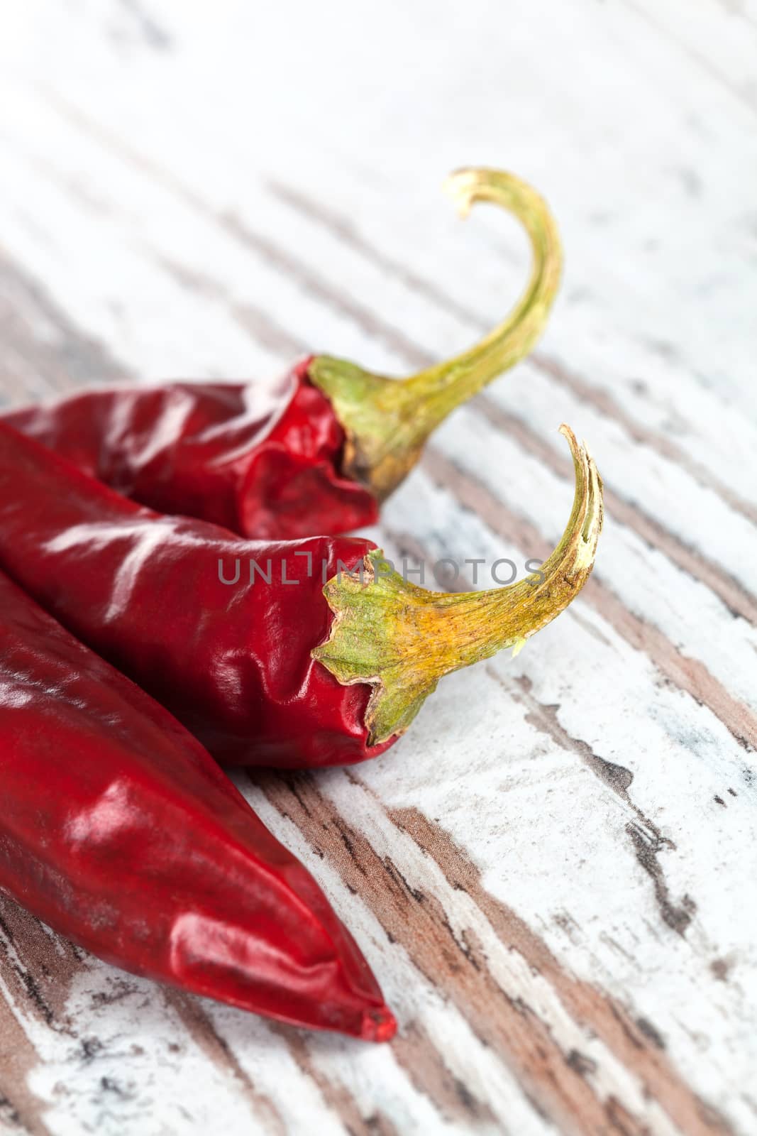 Luxurious chili pepper background. Three dried chili pepper on white wooden textured background. Culinary hot cooking ingredients.