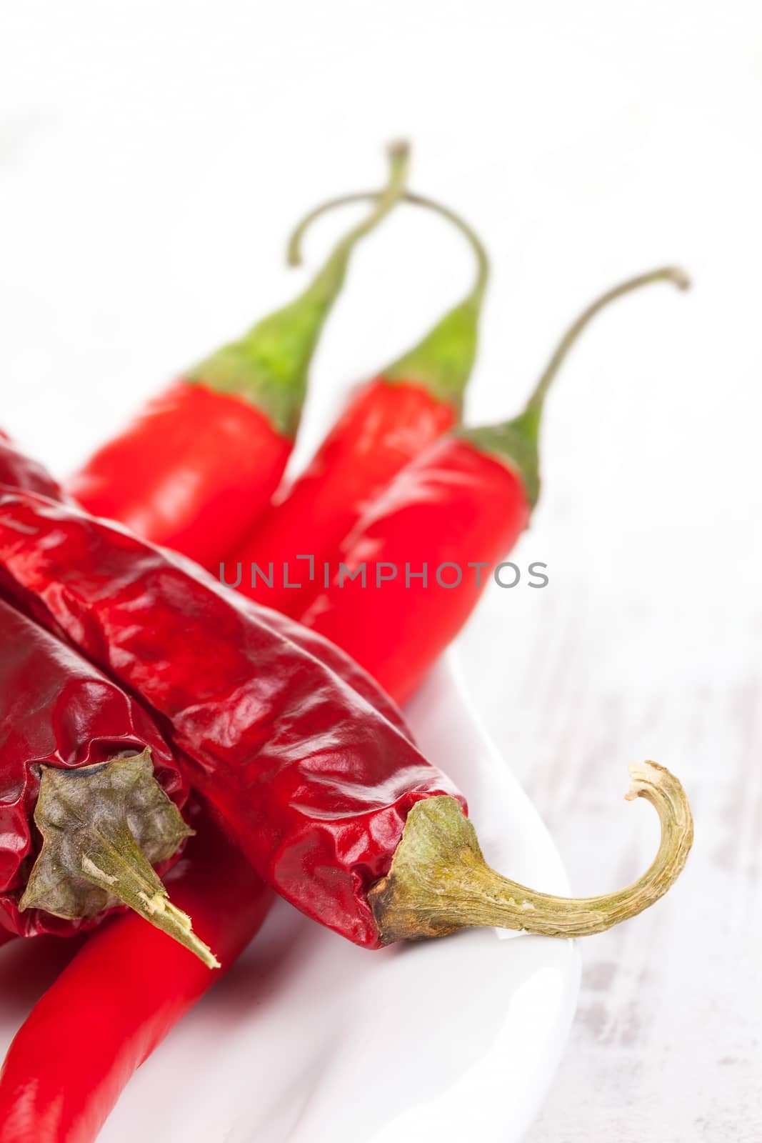 Red hot chili peppers dried and fresh on white plate on white wooden textured background. Culinary hot cooking ingredients.