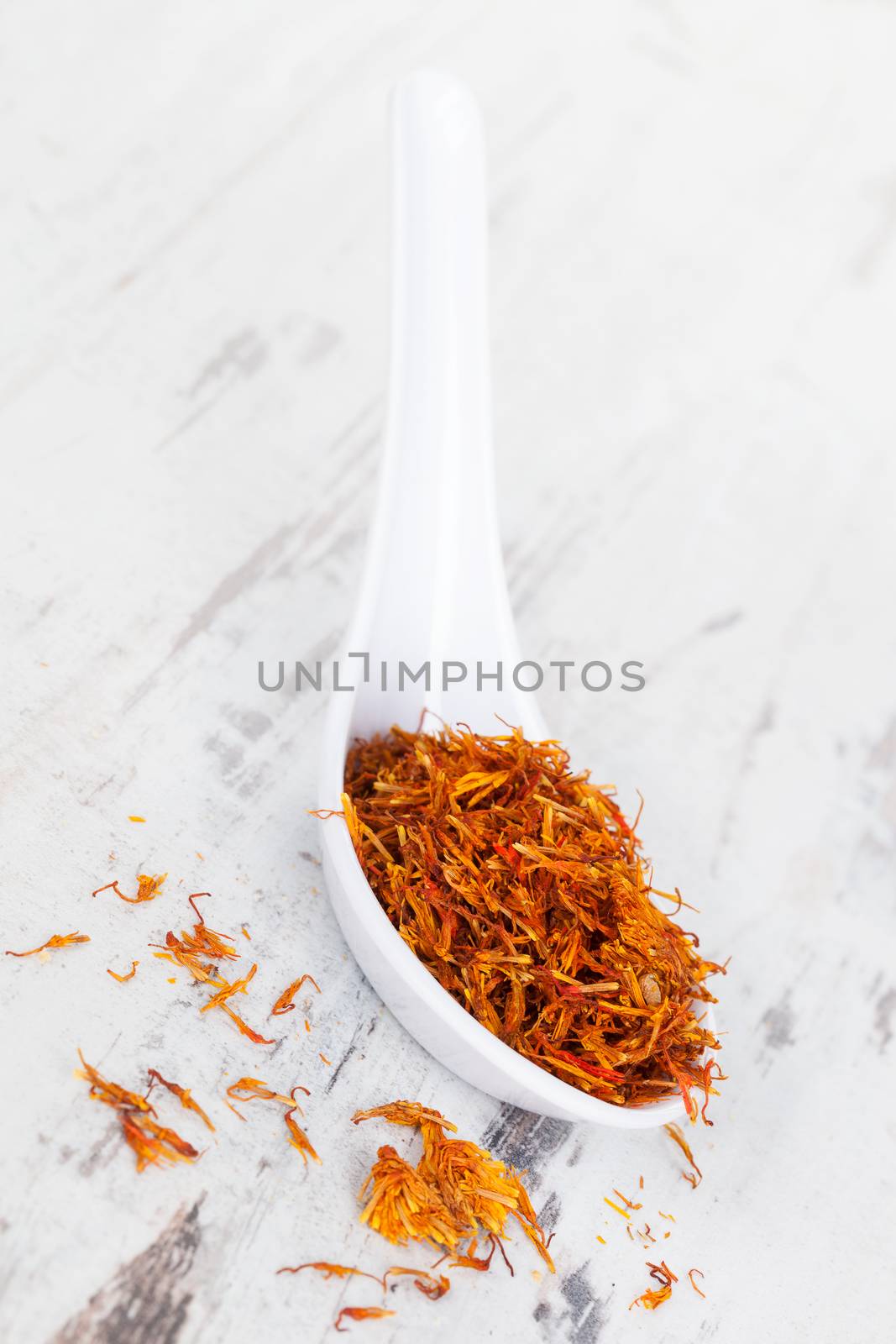 Luxurious saffron spice on white spoon on wooden textured background. Culinary spices.