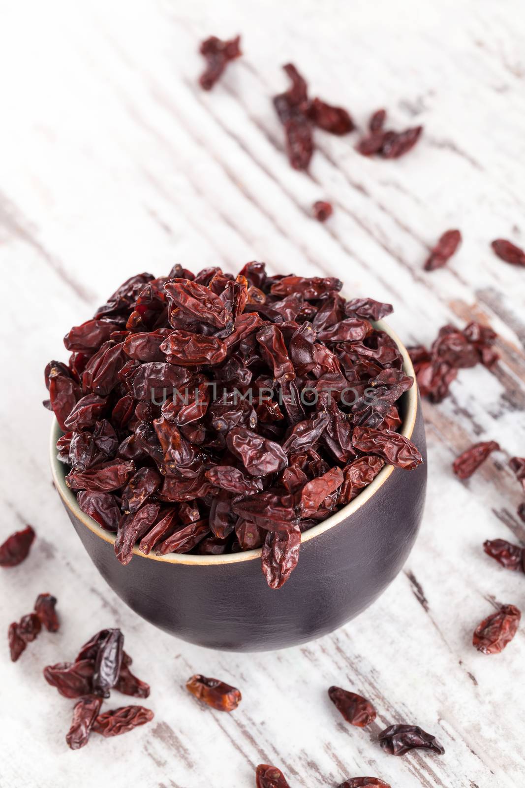 Full bowl of goji on white wooden textured background. Healthy traditional chinese eating supplement.