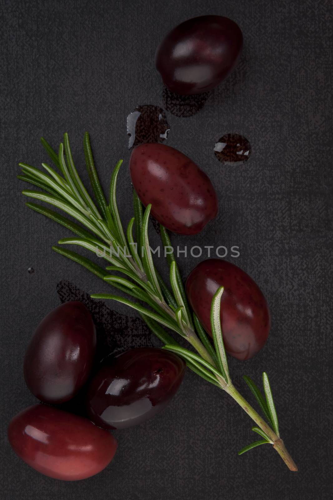 Delicious olive background. Black olives and fresh rosemary herb on black background, top view. Culinary eating.