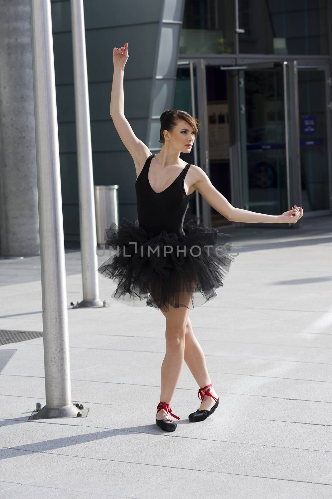 beautiful young ballerina in black tutu taking a classic ballet pose outdoor near a moder building