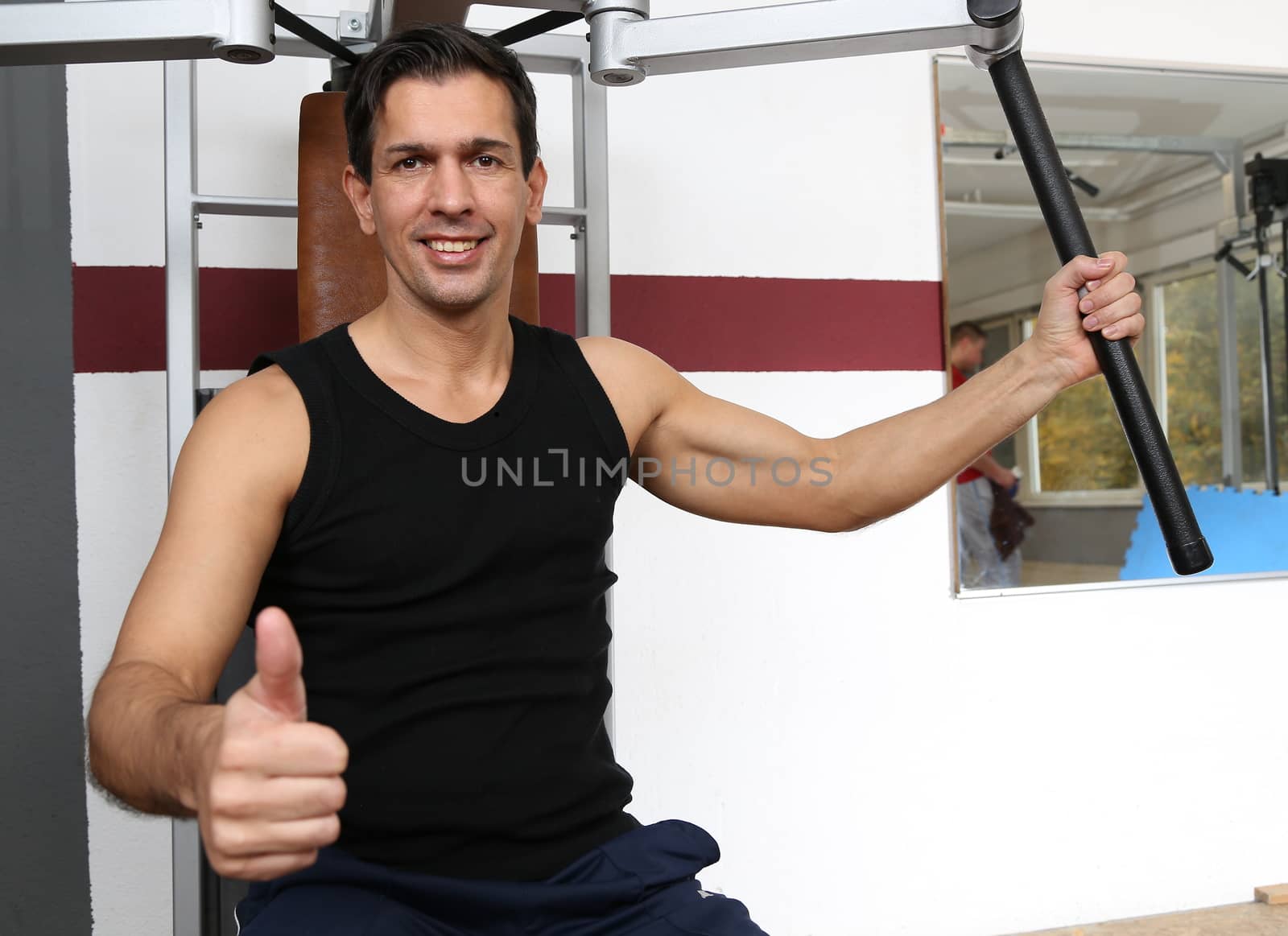 Athletic man exercising and lifting weights in a fitness center showing thumbs up