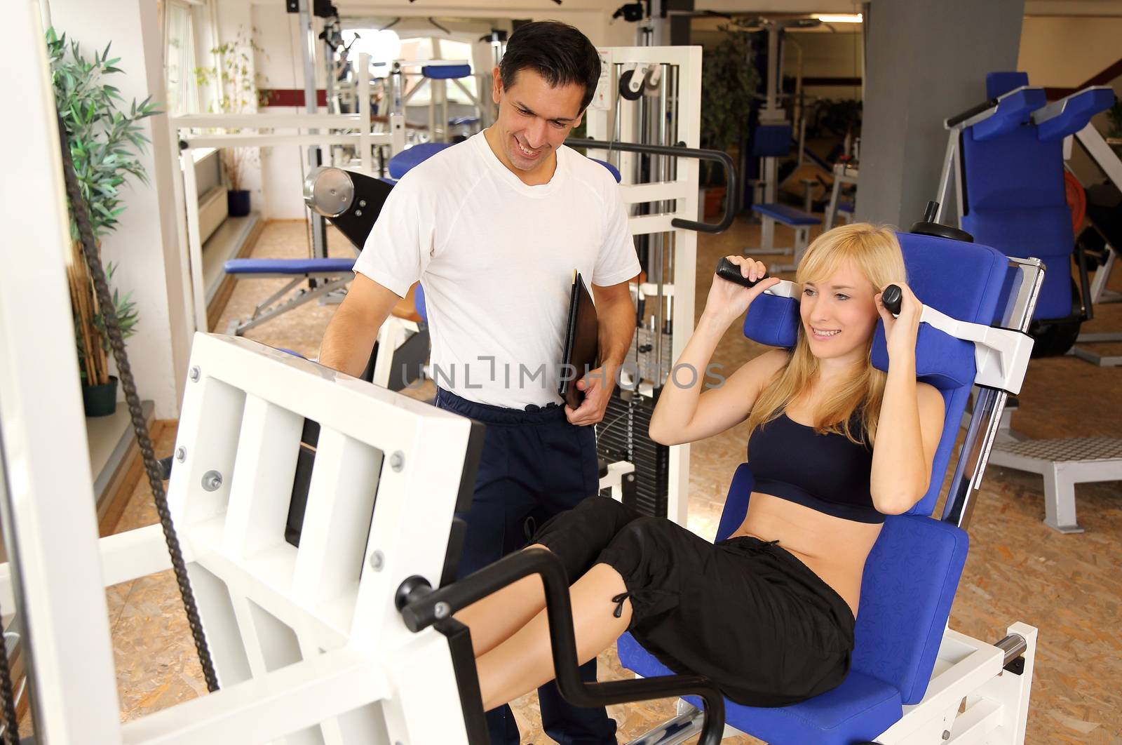 Attractive blonde woman and her trainer in a gym by ikonoklast_fotografie