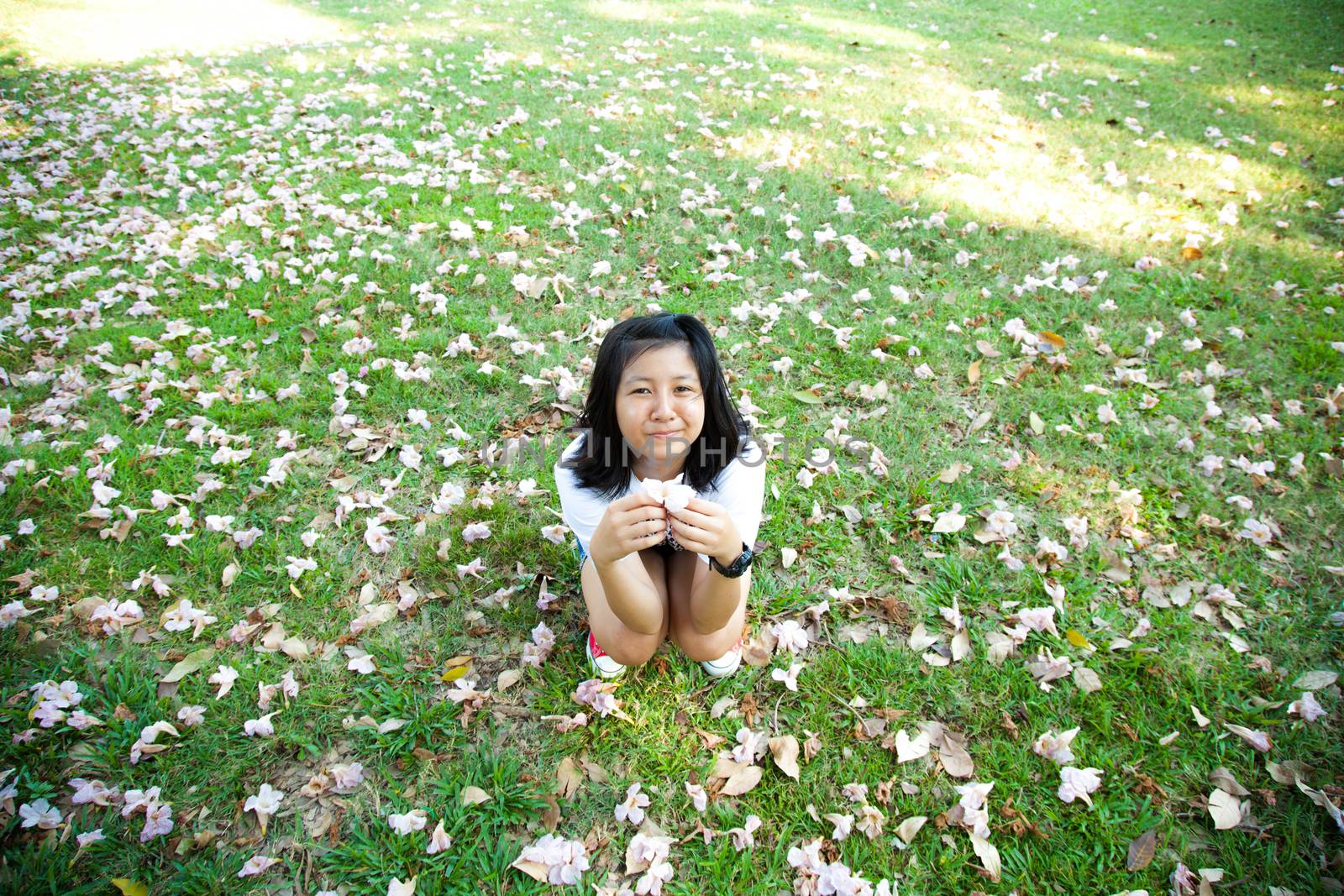 Teenage girl sitting on grass Hands holding flowers. And the blossoms filled the lawn in the park.