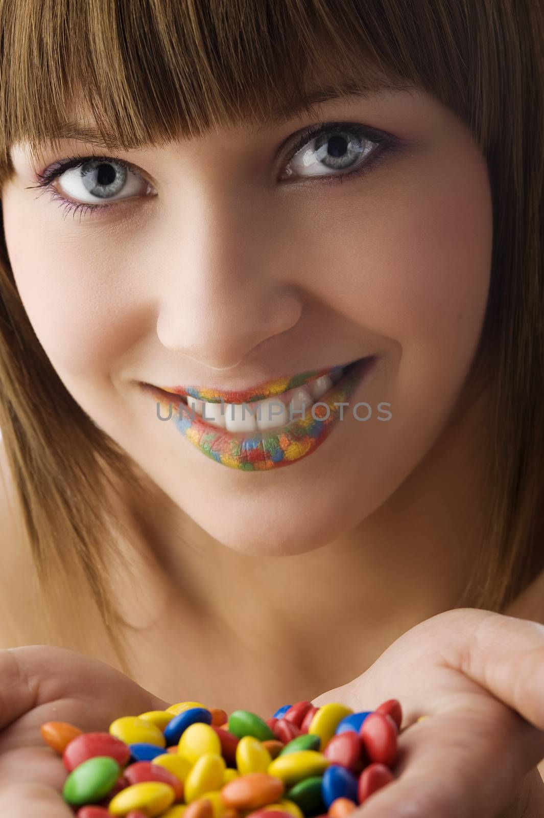 young pretty girl with colored smarties in hand a multi color lips smiling in camera
