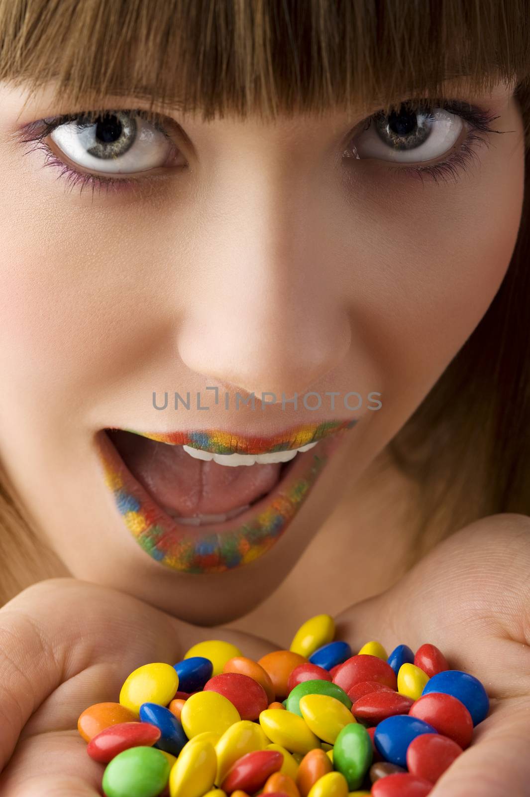 close up of young girl with open colored mouth and a lot of multicolor smarties near