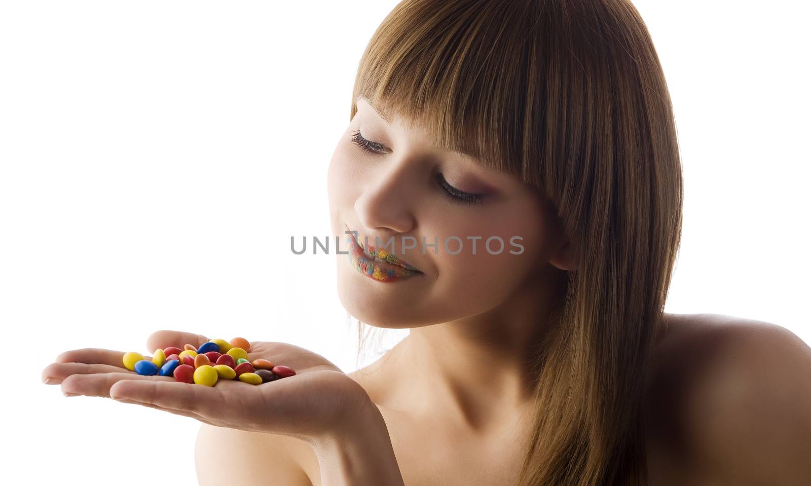 cute girl with multicolor lips in white background loonking some colored candy