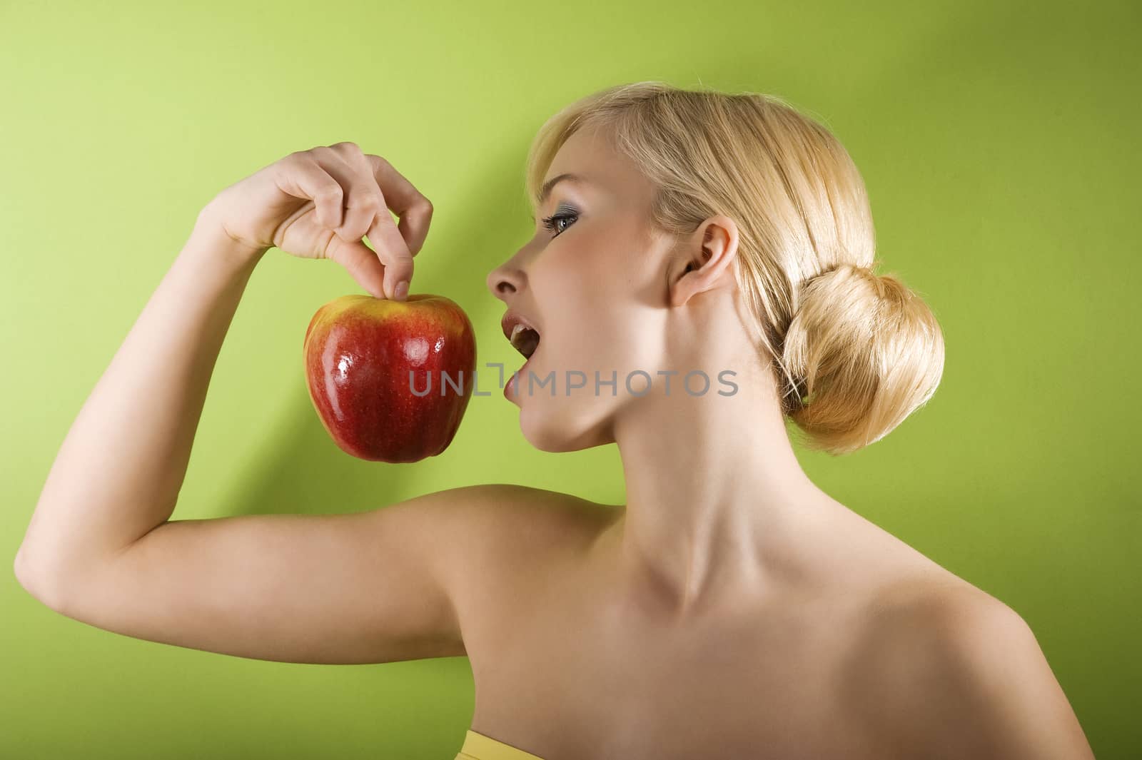 profile shot of blond girl eating a red apple on green background