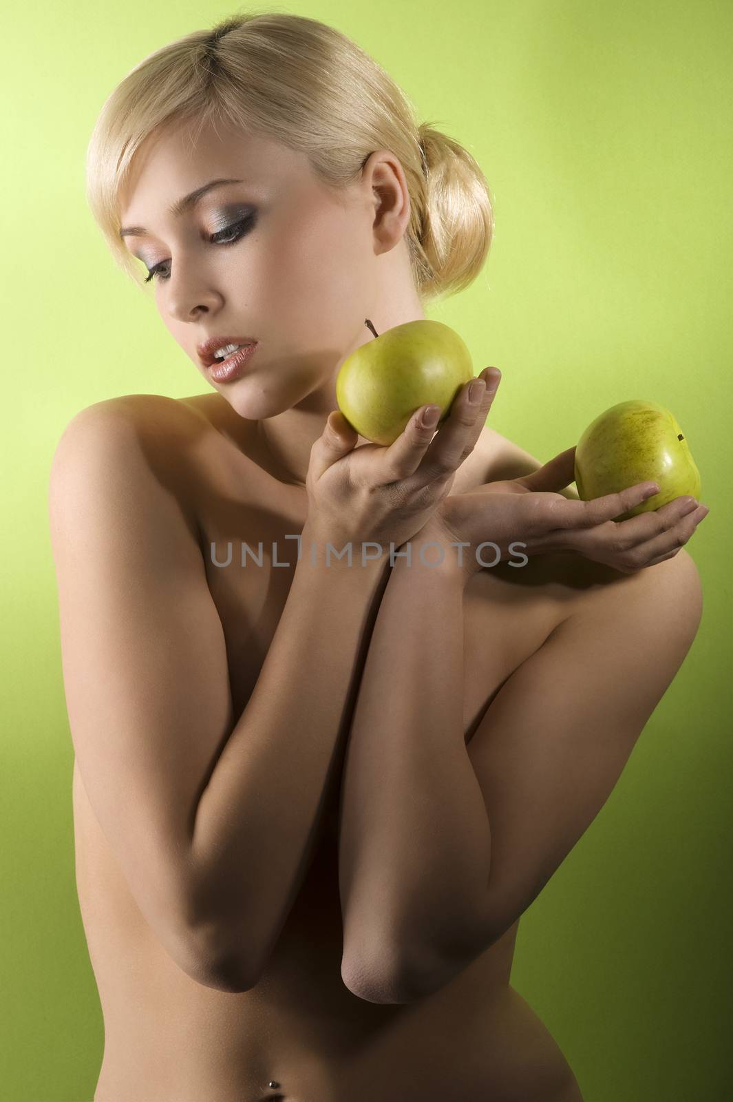 glamour shot of a nude young woman with two apple on green background looking down