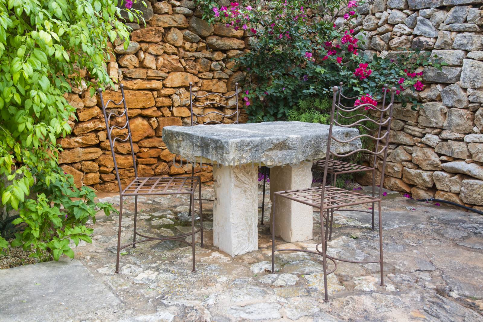 Garden Stone Table with wrought iron chairs, plants and drystone wall.