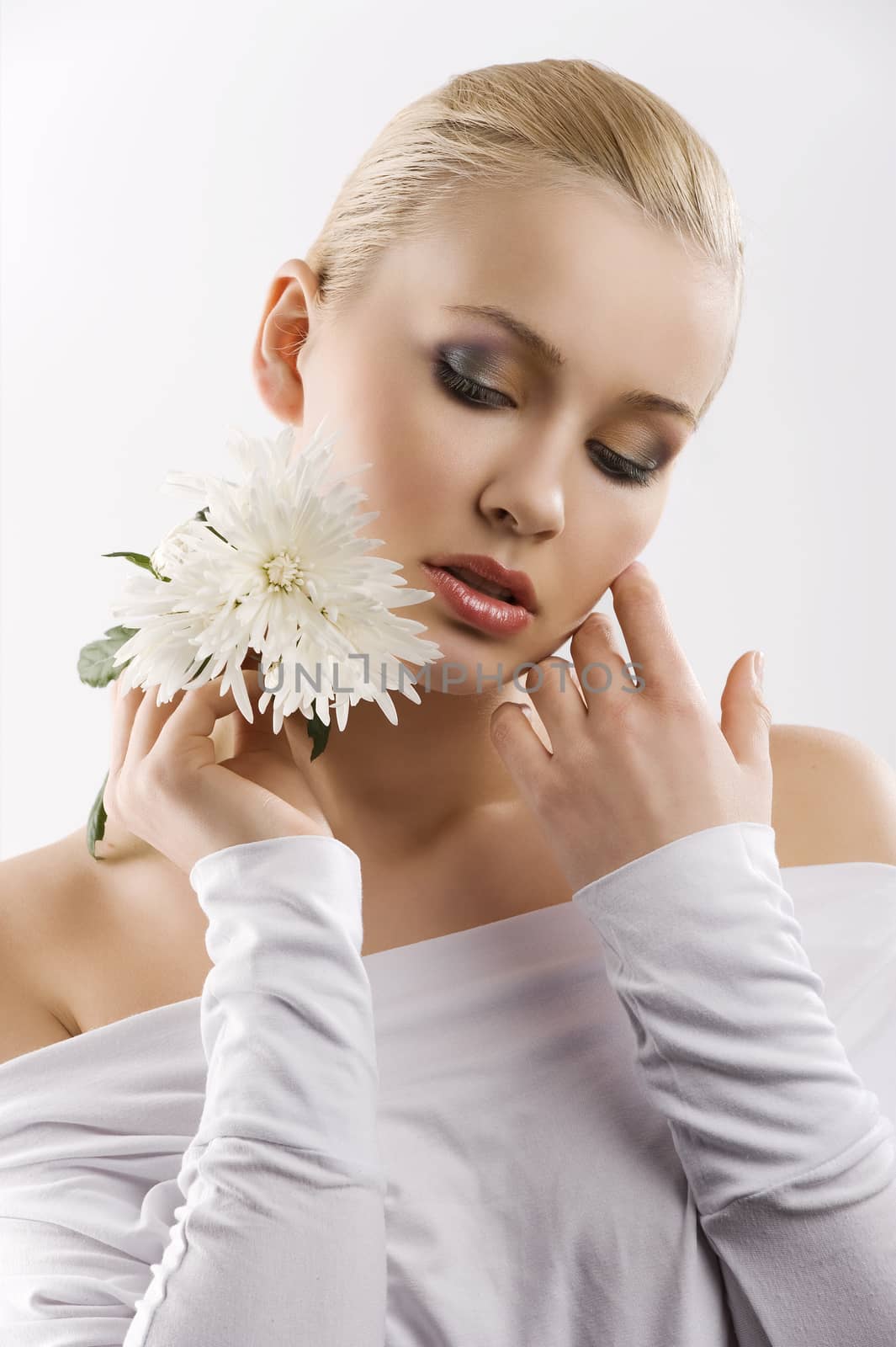 beauty portrait of young cute blond girl with white top and some flowers near face