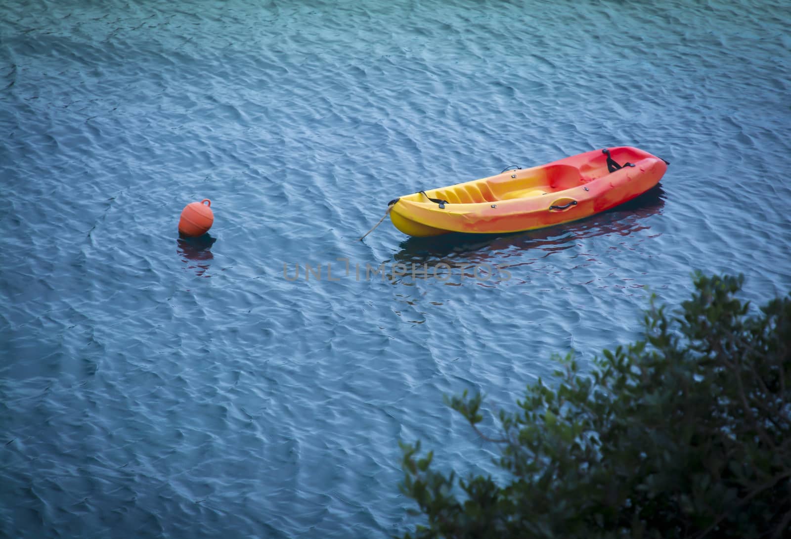 Moored yellow red plastic lifeboat in blue water. Mallorca, Balearic islands, Spain in October.