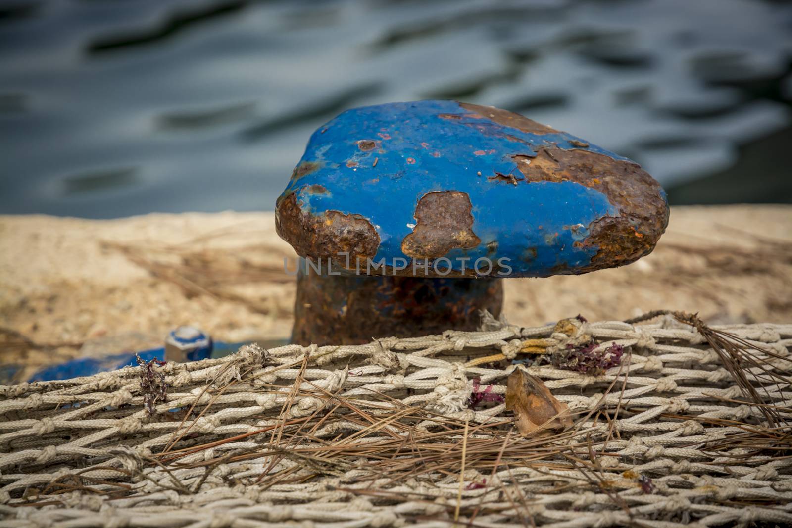Blue Mooring Knob Close-up with rust and flaky paint with fishnet on a jetty, Mallorca, Balearic islands, Spain.